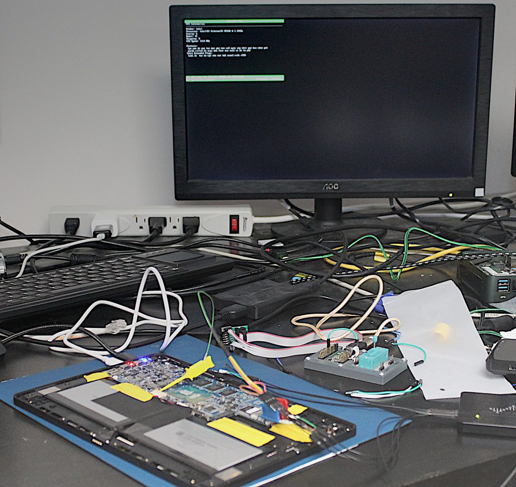 Librem 11, partly disassembled with logic analyzer still attached, displaying coreinfo on an external display